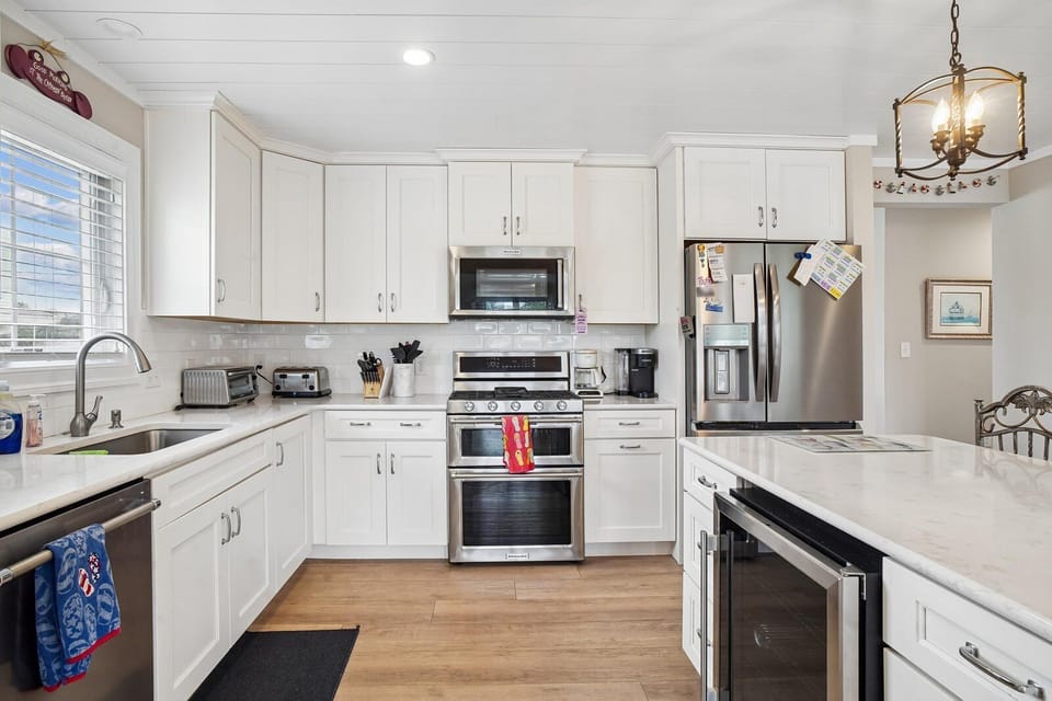 Step into this bright, spotless kitchen where your culinary adventures await—crisp white cabinetry, gleaming stainless appliances, and a spacious center island make every meal a joy to prepare.