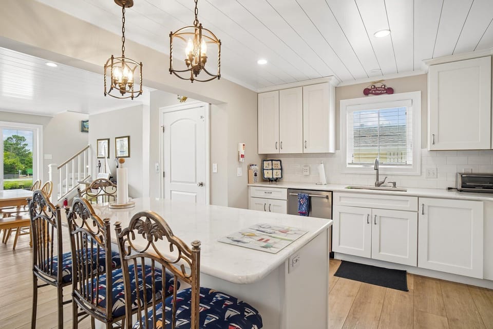 Gather around your bright open kitchen, where crisp white cabinetry, warm wood floors, and elegant pendant lighting create the perfect space for cooking and sharing meals together.