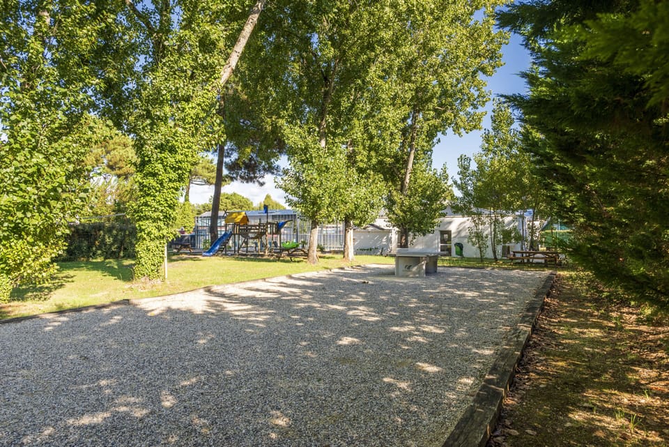 Walk the gravel path past the pétanque court toward the shaded playground.