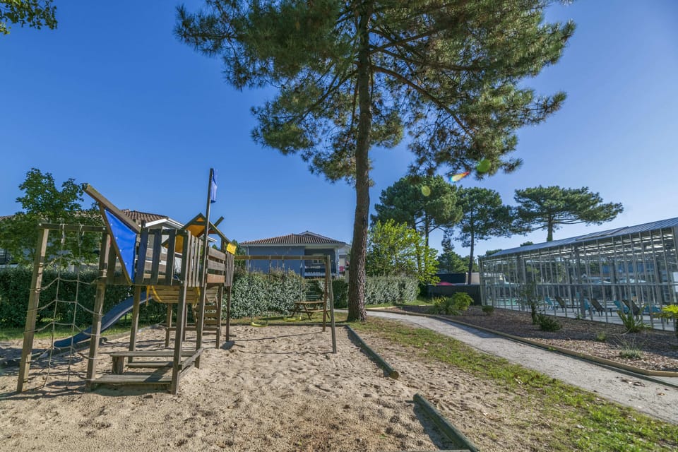 Kids can climb the wooden playground set in sand beneath tall pines.