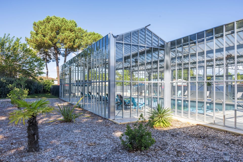 The glass-walled pool pavilion sits behind gravel landscaping dotted with palms.