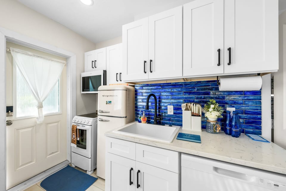 The kitchen is fully equipped for real meals: full electric range and oven, microwave, retro-style refrigerator with freezer, deep sink, quartz countertops, cookware, utensils and a striking cobalt glass backsplash.