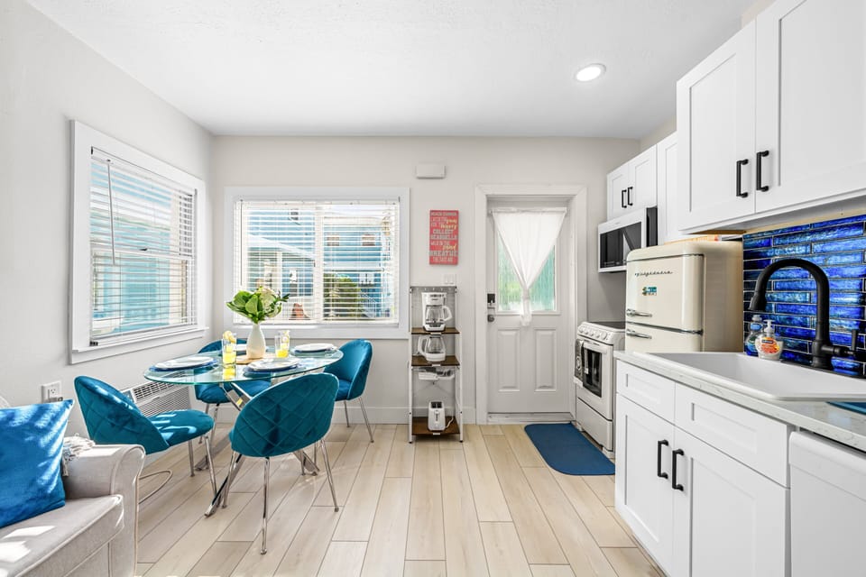 Cook in beach-house style — a complete kitchen with full oven and range, retro refrigerator, microwave, dishwasher, quartz counters and a cobalt glass-tile backsplash, opening straight onto the dining nook.