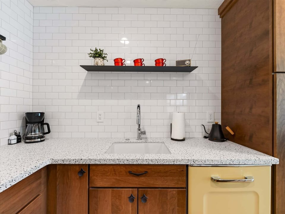 A retro-inspired kitchen with modern convenience, featuring warm wood cabinetry, vintage-style appliances, quartz countertops, and open shelving. Fully stocked with cookware, utensils, and everything you need to prepare meals with ease.