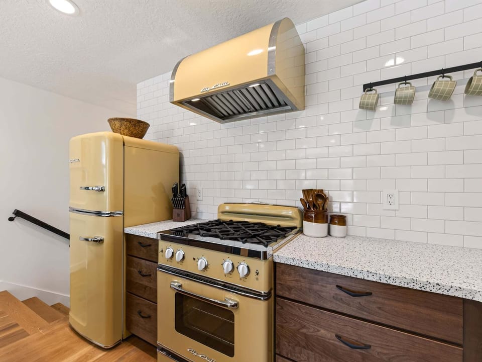 A retro-inspired kitchen with modern convenience, featuring warm wood cabinetry, vintage-style appliances, quartz countertops, and open shelving. Fully stocked with cookware, utensils, and everything you need to prepare meals with ease.
