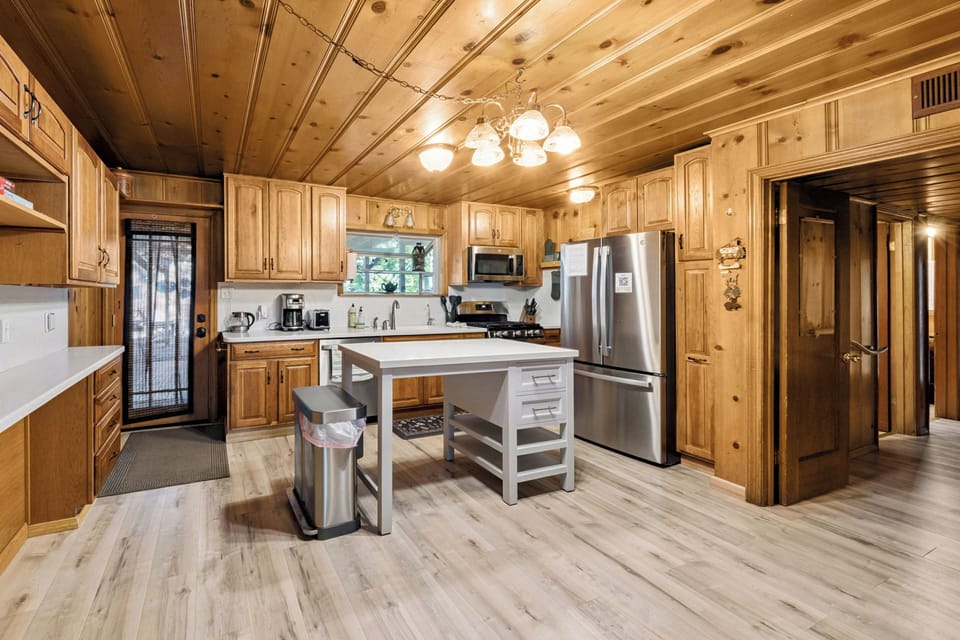 Fully equipped kitchen offering bright white cabinetry, stainless steel appliances, a central prep island, and warm pine paneling.