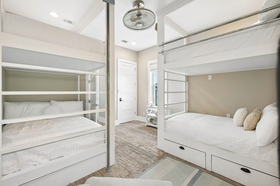 Rest easy in this airy bedroom featuring a cozy bunk bed and a comfortable queen bed, both styled in calming neutral tones. Your whole crew can unwind here after a day of adventure.