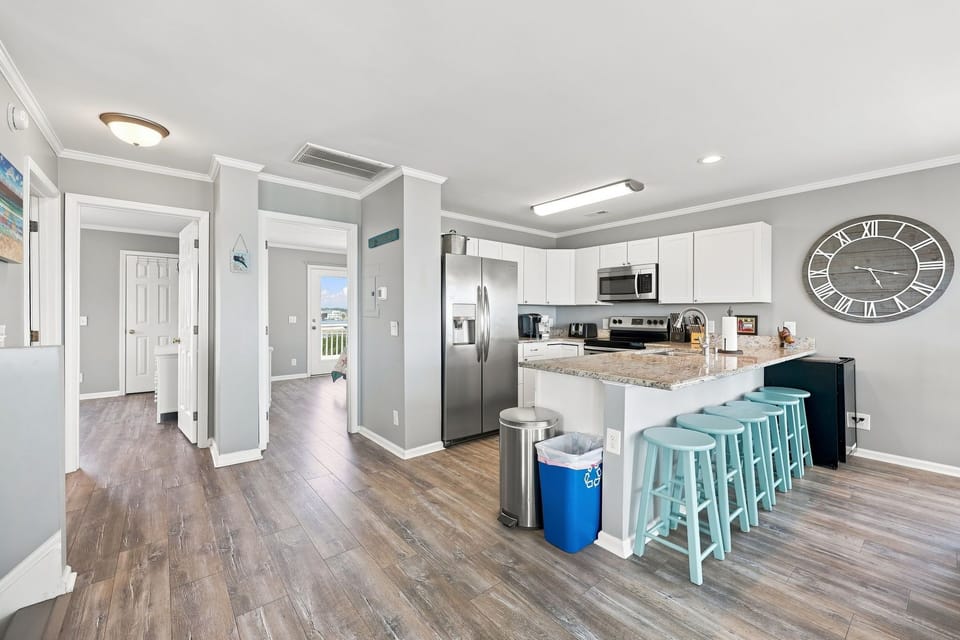 The expansive great room offers wood-style floors, sleek grey walls, and a stunning perspective of the kitchen, dining, and living areas.