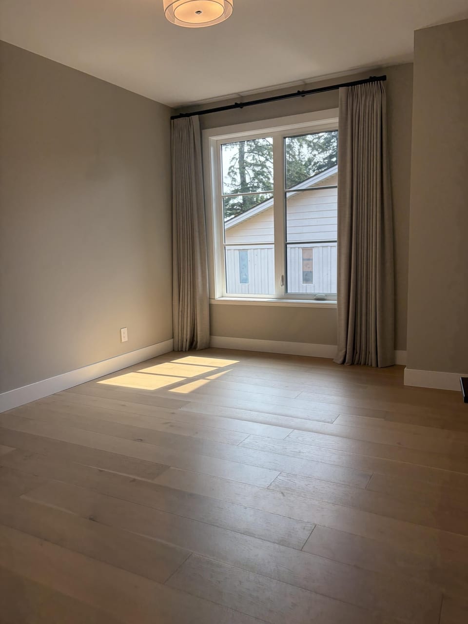 Tall windows filter warm sunlight into this serene guest bedroom retreat.