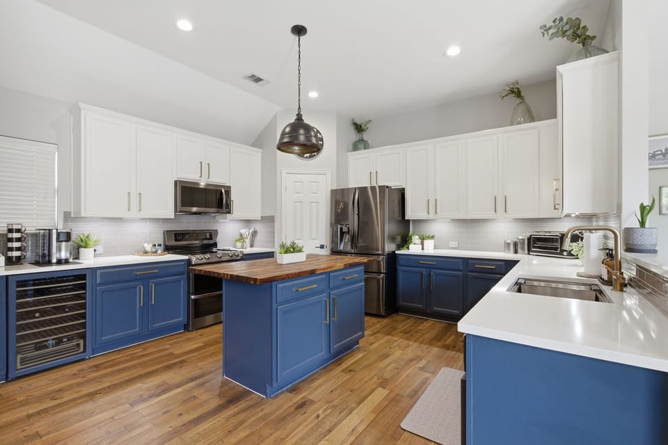 Fully equipped Kitchen with a large butcher-block Island, navy cabinetry, hardwood floors, and stainless steel appliances. Perfect for cooking up a Texas-sized meal.
