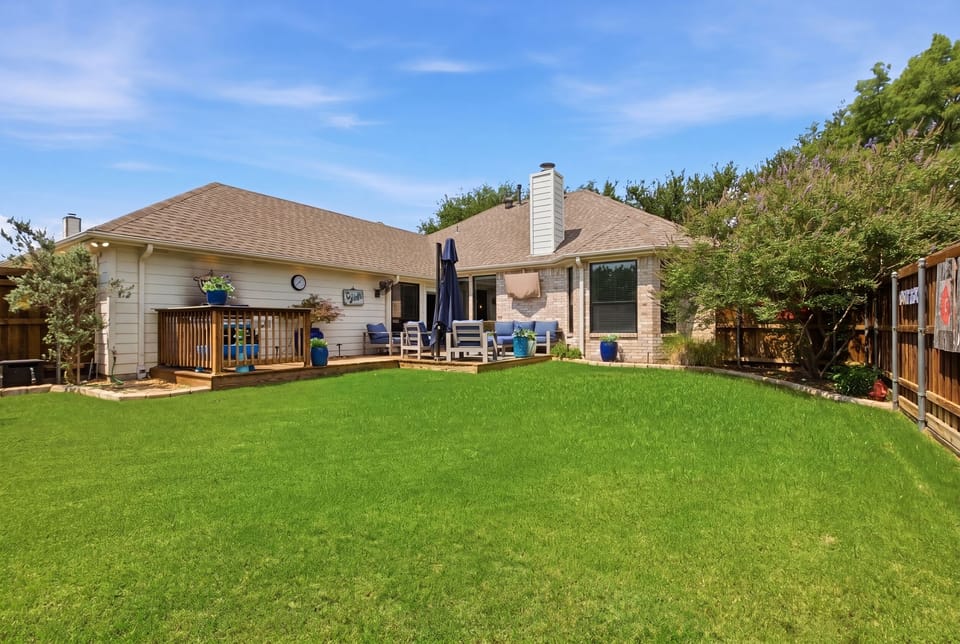 Spacious lawn and wooden Patio with comfortable Outdoor Furniture, navy cushions, and a large umbrella. Ideal for morning coffee or evening grill-outs near Grandscape and Frisco.