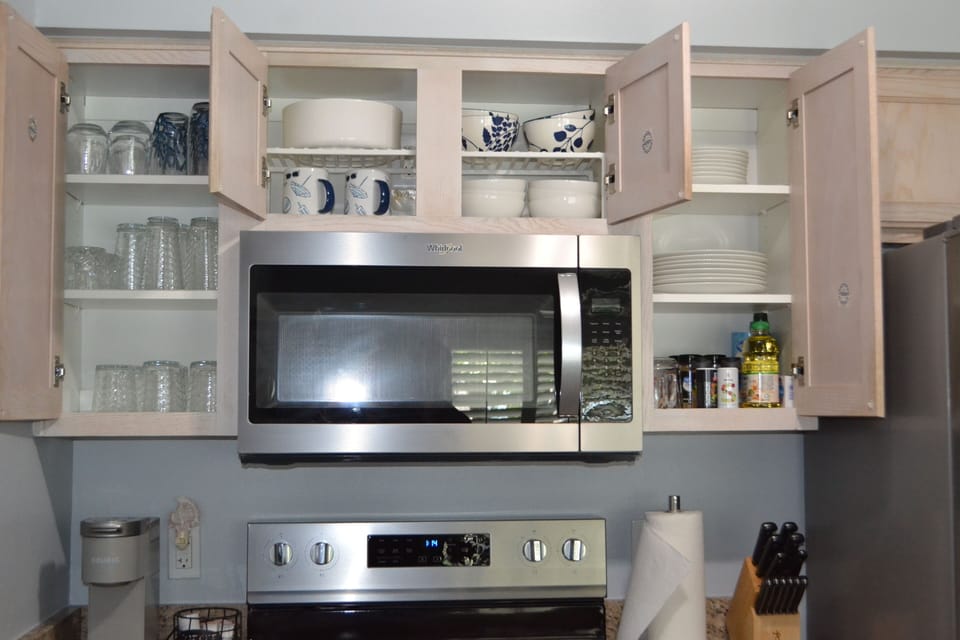 Fully stocked kitchen with plates, bowls, silverware, glasses, coffee mugs.