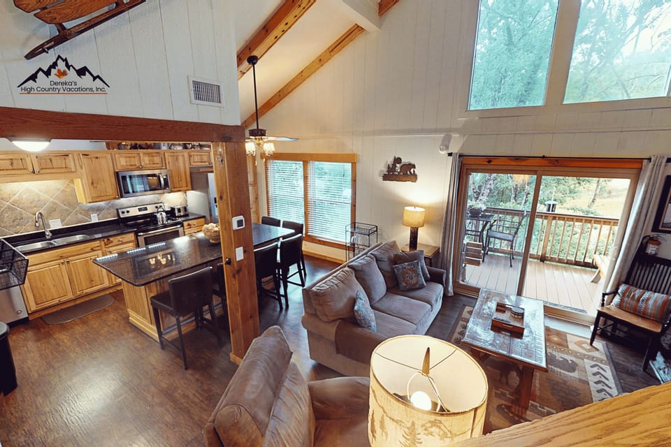 Step into your mountain retreat where vaulted ceilings and natural wood beams create an airy, welcoming space. Your open layout connects the full kitchen to a cozy living area, with a private deck framed by forest views inviting you to unwind.