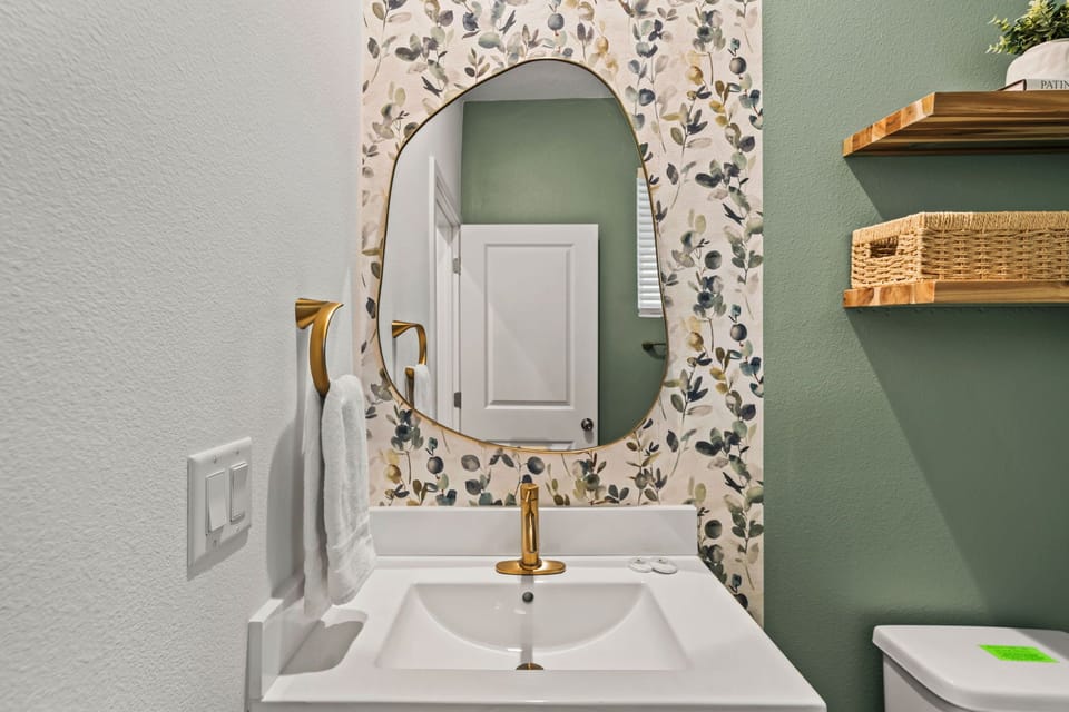 A charming powder room with soft botanical wallpaper, sage-green walls, and gold accents adds a stylish, spa-like touch to the home.