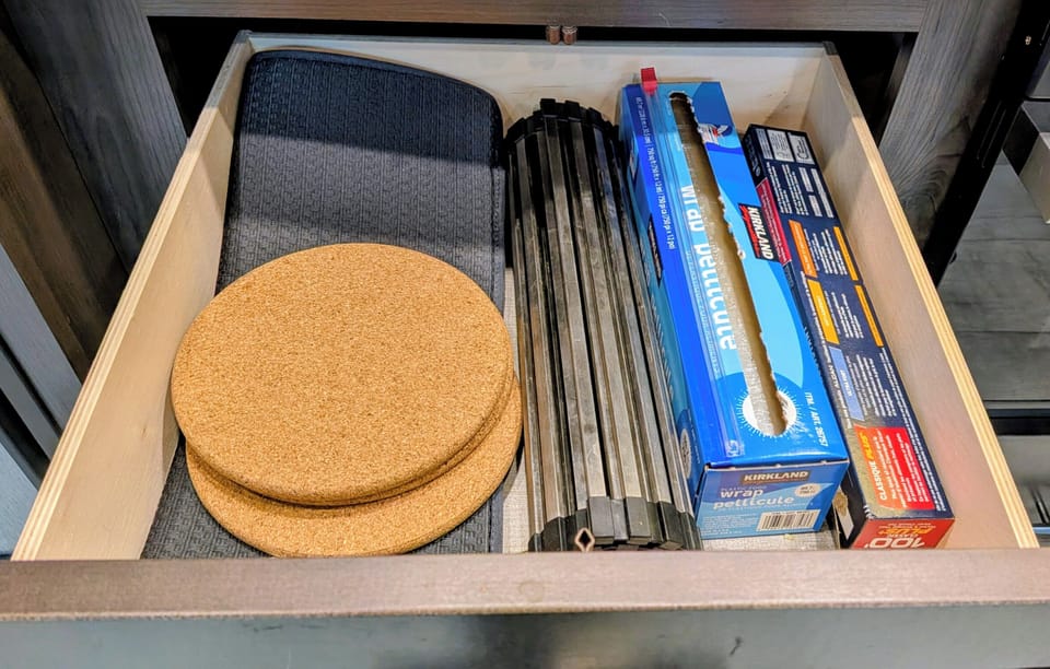 Well-stocked kitchen drawer with wraps, trivets, and roll-up drying rack.