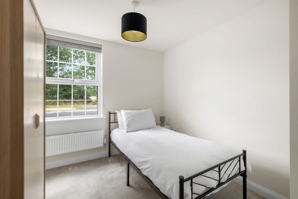 Bedroom 5 is a downstairs cosy single room with a chest of drawers for storage, a bedside light, and a freestanding fan, a quiet spot for a solo guest or extra member of the group.