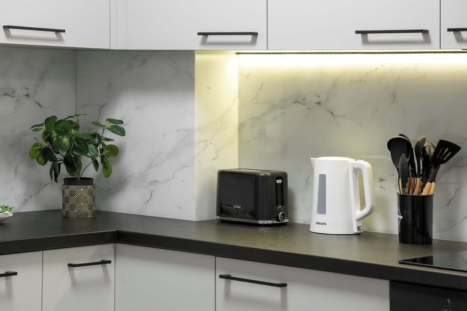 A compact kitchen with white cabinetry, a dark refrigerator, and a built-in oven. The adjacent dining table is neatly arranged with tableware.