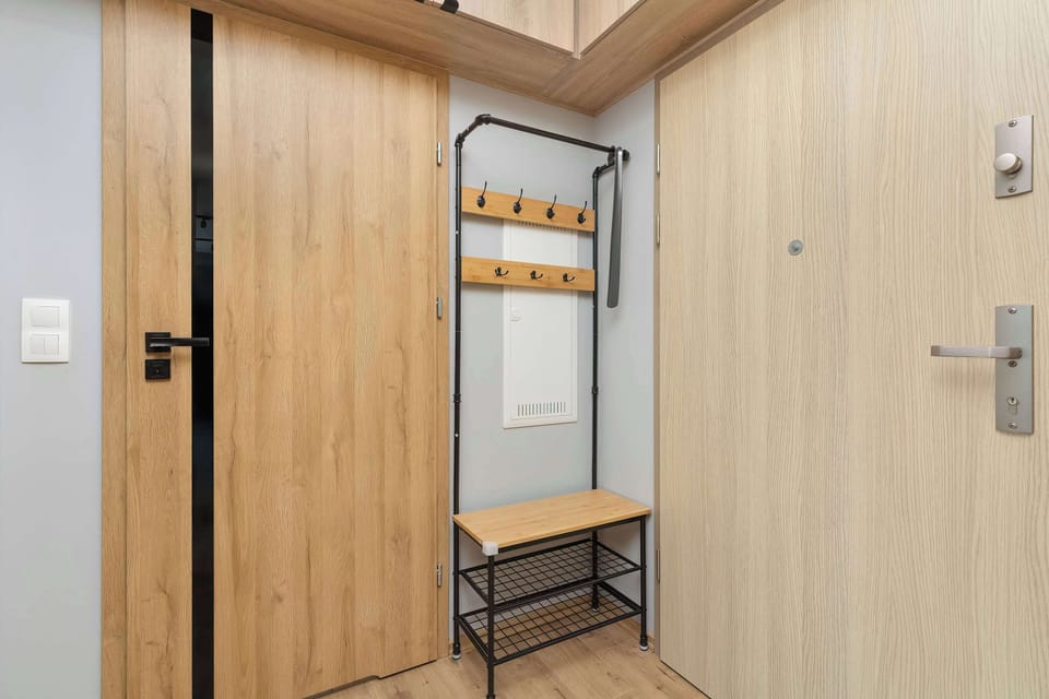 The apartment entrance hall features an integrated coat hanger, bench, and secure entry door. Warm wood paneling and minimalist hardware maintain an organized, uncluttered entryway. Bright overhead lighting welcomes guests upon arrival.