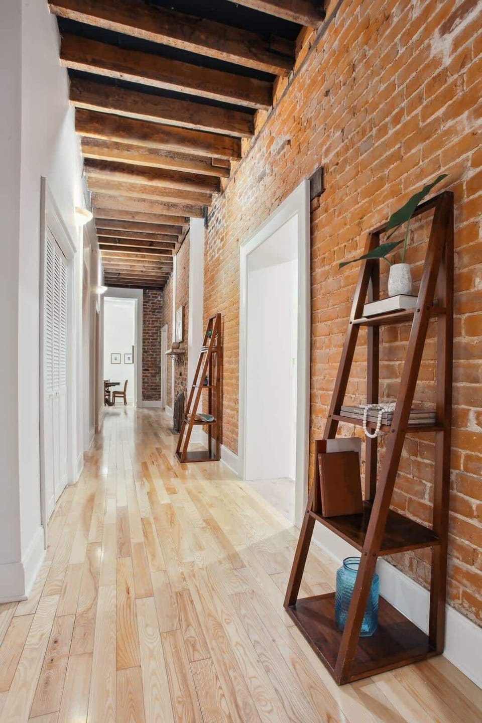Hall | Interior Hallway Connecting Bedrooms with Exposed Beam Ceiling and Brick Wall | Third Floor of Building — Unit on One Level