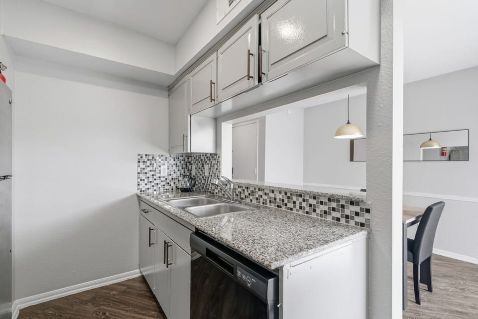 Private kitchen with granite countertops, a mosaic tile backsplash, double stainless-steel sink, dishwasher, and convenient pass-through to the dining area.