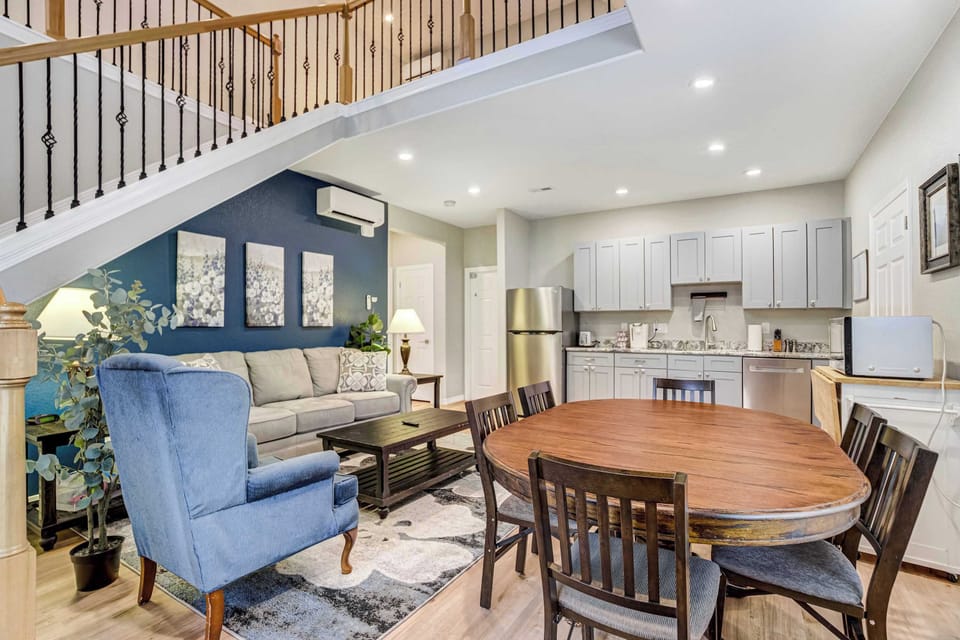 The pedestal dining table gathers everyone beneath warm recessed lighting, with a blue accent chair tucked nearby for anyone who prefers to linger. An easy spot for card games, morning coffee, or a slow shared breakfast