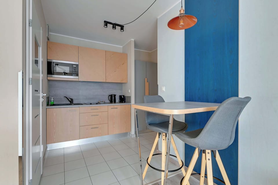 Dining area with a small round table and two chairs. The table is placed near a blue accent wall and a hanging light, making the area stylish and inviting.