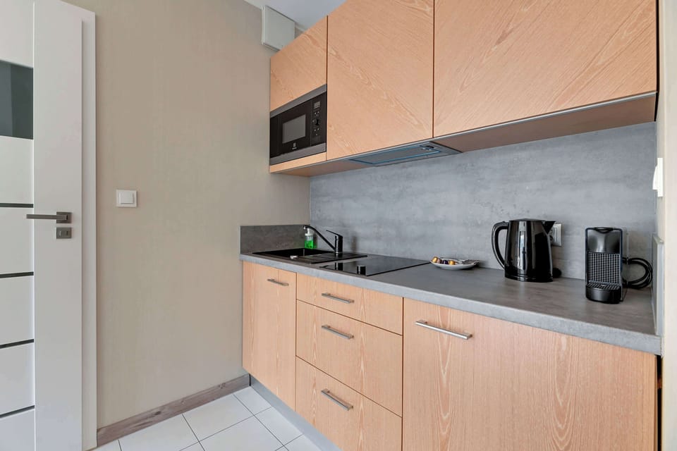 Compact kitchenette with light wood cabinetry and a microwave. The design is minimalistic and efficient, perfect for small-space living.