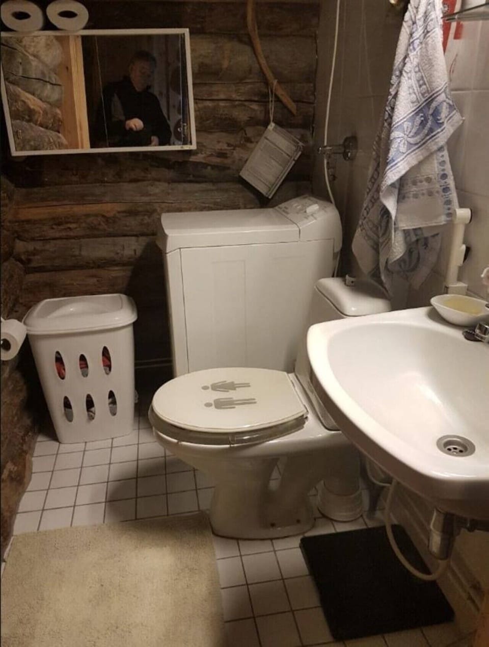 Bathroom with a toilet and washbasin, finished in tile and log.