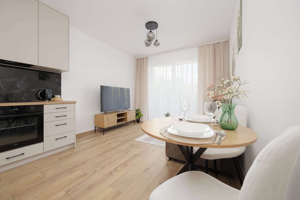 Modern living room with a comfortable beige sofa, a round dining table with chairs, a TV and large windows.