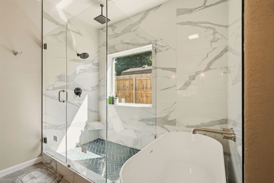 Large primary walk-in shower has rain head and regular shower head, small bench for shaving and a large window (which actually has a covering although not pictured).