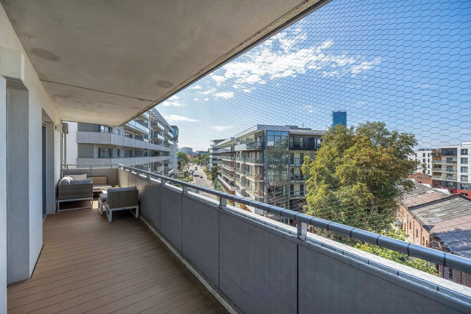 Spacious balcony with outdoor seating and a small table, offering views of the surrounding buildings and greenery.