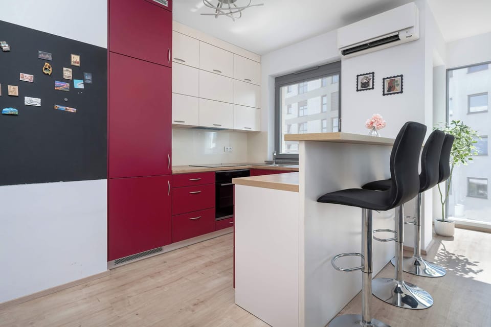 Modern kitchenette with red and white cabinets, a countertop, a sink, a cooking area and a breakfast bar with high chairs.