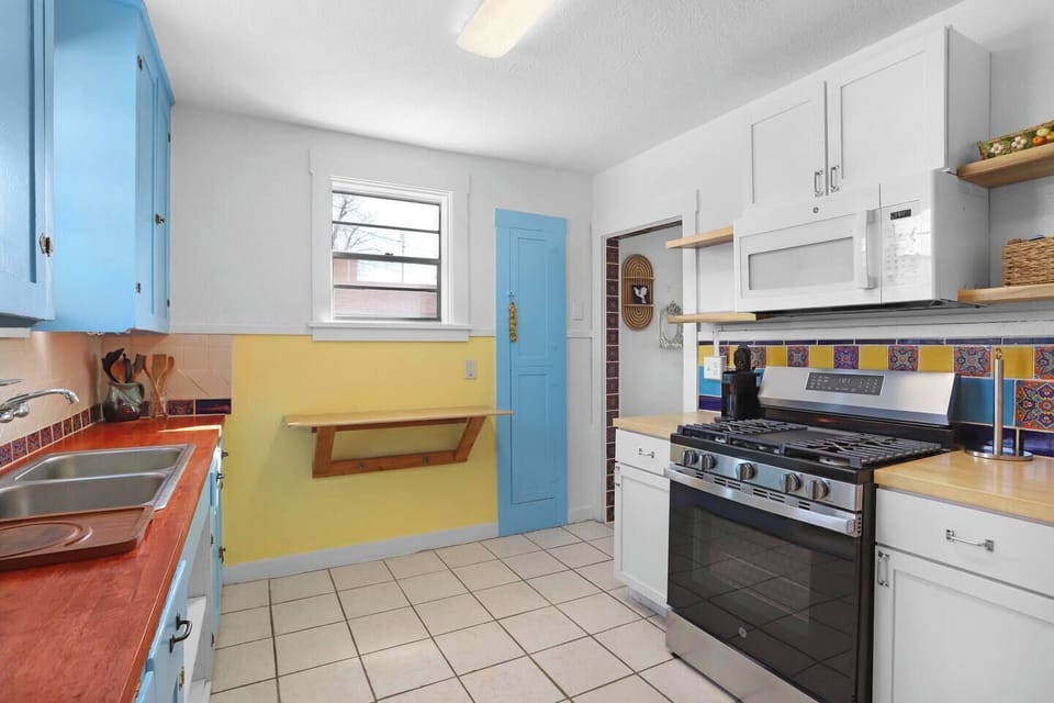 Sunny, cheerful kitchen with pops of blue and yellow, a full-size gas range, and colorful tile accents. Thoughtfully designed with open shelving and ample counter space—ideal for relaxed mornings and easy home cooking.