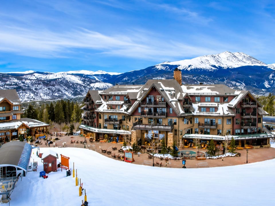 A stunning mountain resort property set against snow-capped peaks and evergreen forests, providing a scenic arrival experience in a pristine alpine setting.