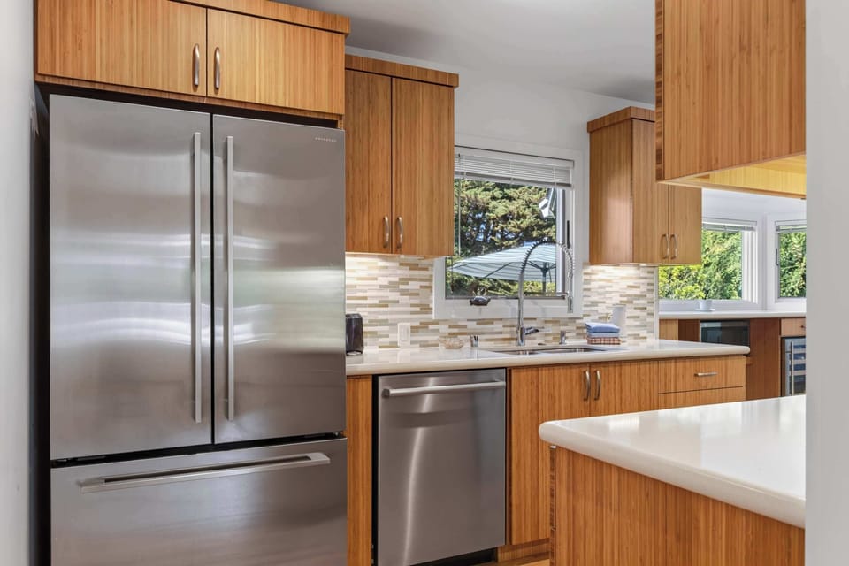 Stainless French-door fridge, dishwasher, and deep sink line one wall of the galley kitchen, all wrapped in warm vertical-grain cabinetry.