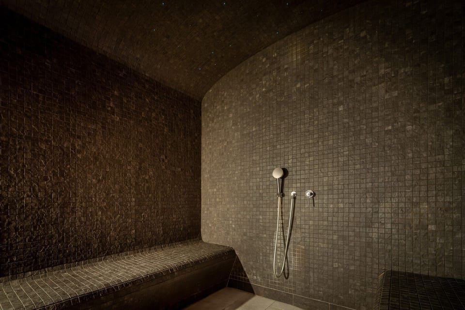 Dark tiled steam room with benches and shower fixtures.