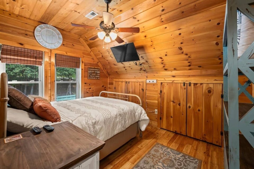A bright queen bedroom featuring floor‑standing shelving, a smart TV, and a ceiling fan—comfortable, simple, and ideal for restful nights.