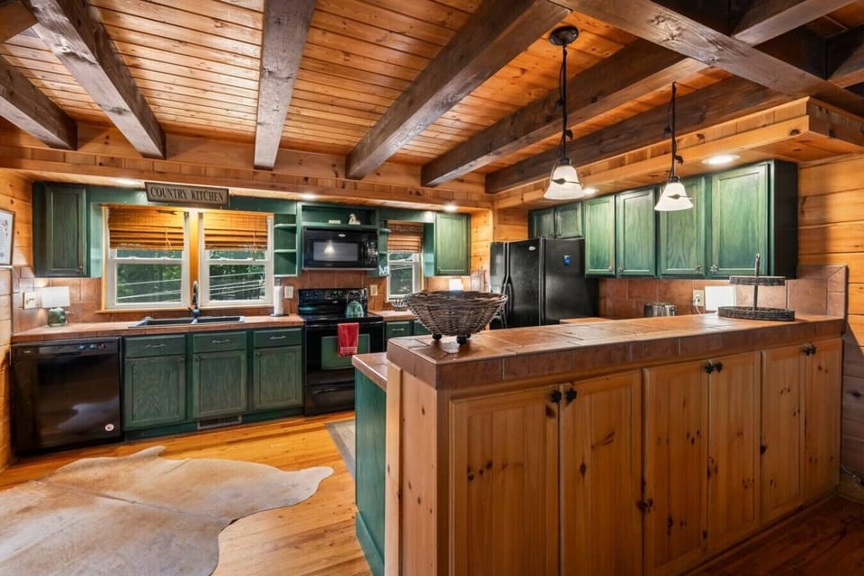 A warm, cabin‑style kitchen with a double‑door fridge, dishwasher, microwave, and a spacious bar area—perfect for gathering after long days at TIEC or exploring the mountains.