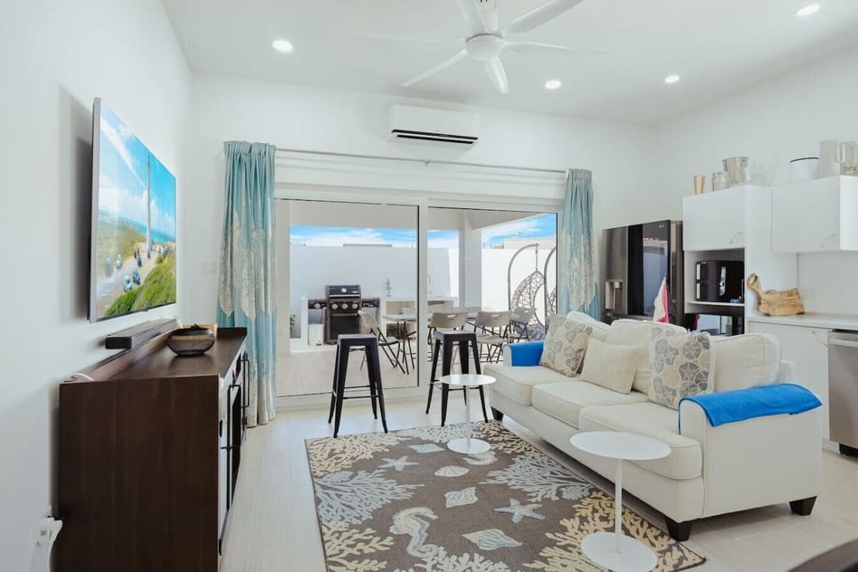 Open-plan living area with a comfy sofa, TV, and full kitchen, with the patio just steps away for easy indoor-outdoor living.