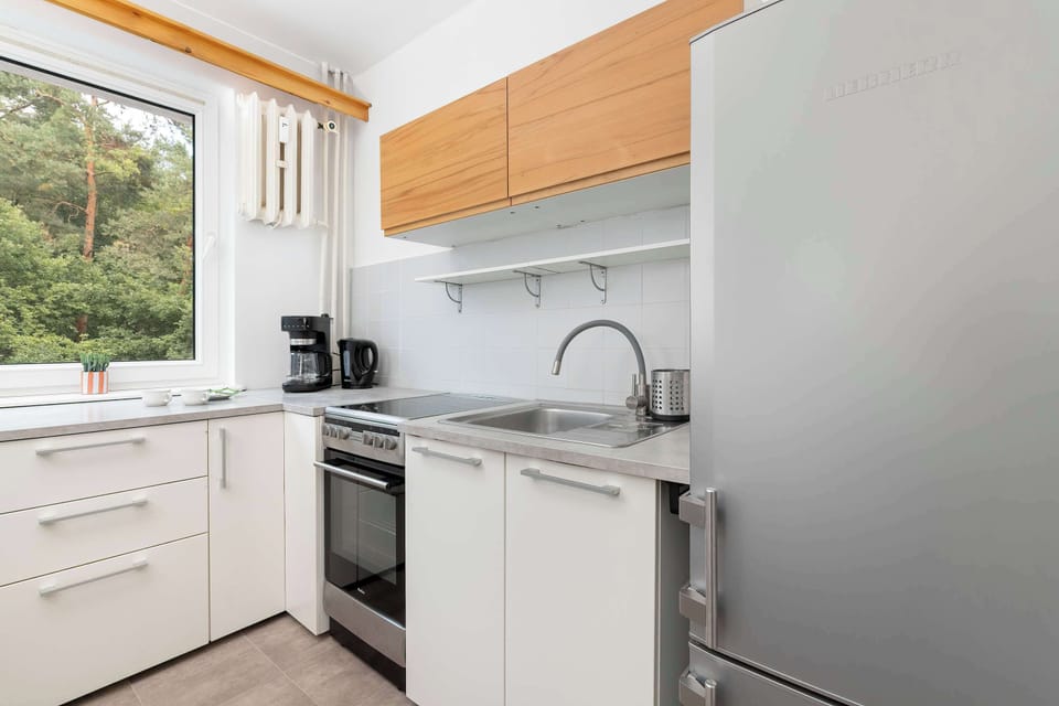 A compact kitchen is fitted with white lower cabinets and wooden upper cabinets. A modern stainless steel refrigerator stands at the end of the counter.