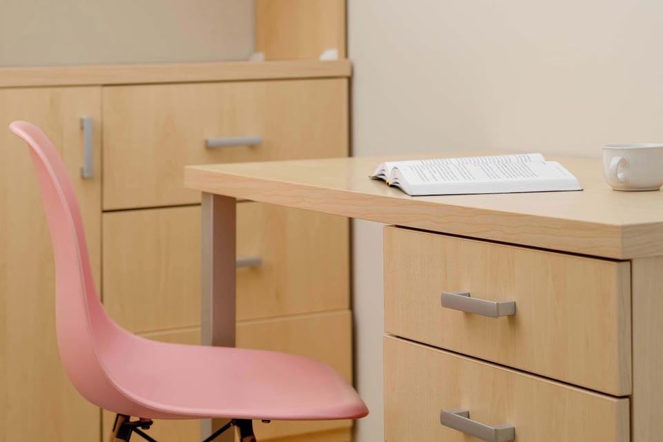 A closer view of a wooden desk reveals a neat workspace with storage drawers. A vibrant pink chair is positioned ready for use.
