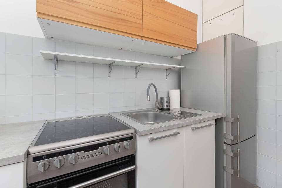 A modern kitchen space features a stove, sink, and contrasting white and wood cabinetry. A stainless steel refrigerator fits snugly at the end of the counter line.