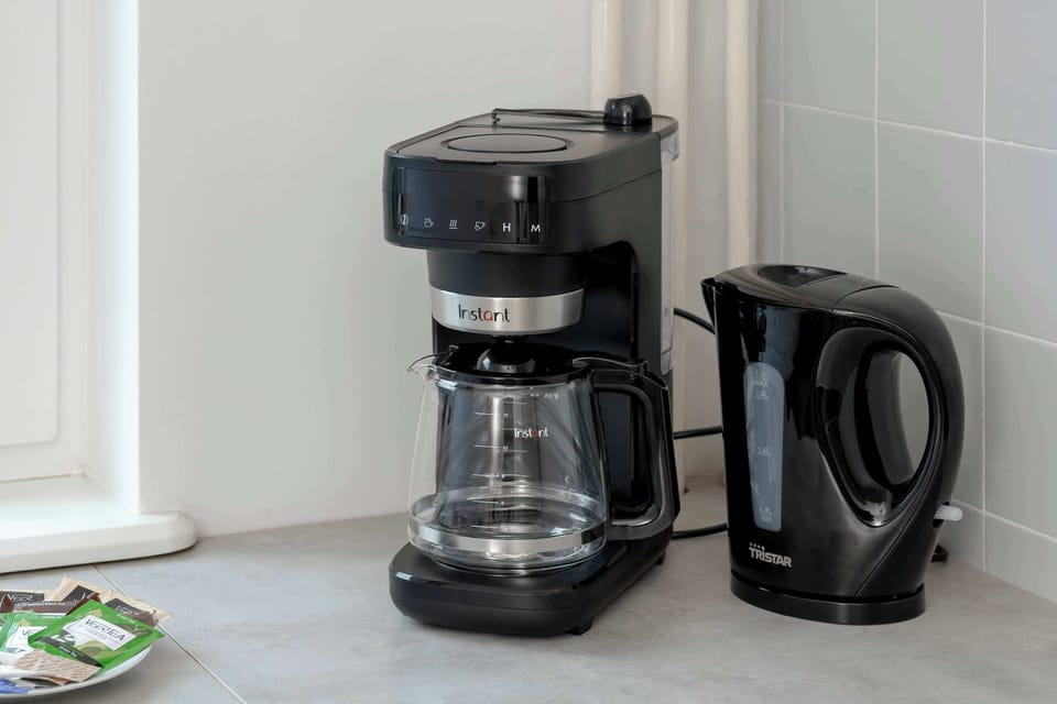 A black coffee machine and a matching electric kettle are positioned on a grey countertop. They stand ready for brewing hot beverages.