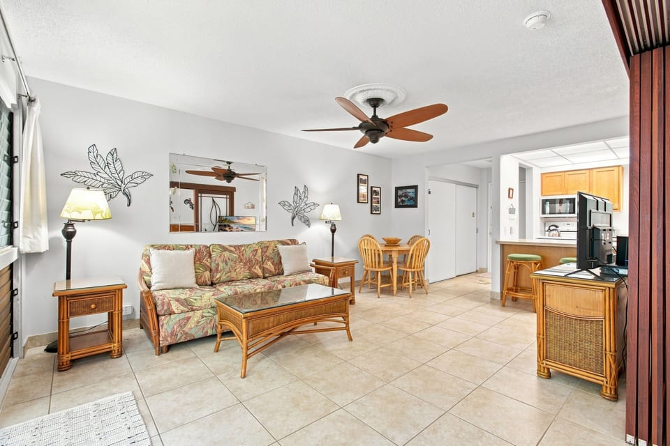 Settle into your comfortable living room with tropical-inspired furnishings and breezy ceiling fans overhead. The open layout flows seamlessly into your dining area and full kitchen, creating a welcoming retreat.
