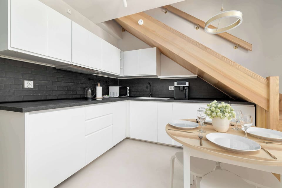 The kitchenette area offers ample dark countertop space paired with minimalist white cabinets. A round dining table sits conveniently adjacent to the exposed wooden roof structure.