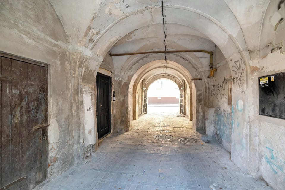 A vaulted stone archway forms the building's historic entrance passage leading through toward the sunlit street. The rustic masonry and arched ceiling highlight the historic charm of the property.