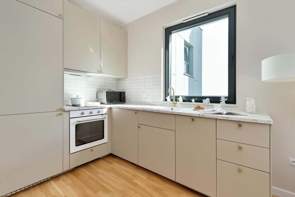 Modern white kitchenette with wooden floors and a window.
