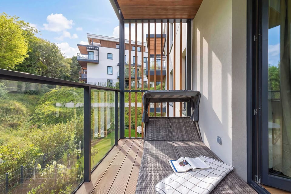 Balcony with a chair, wooden floor, and greenery outside.