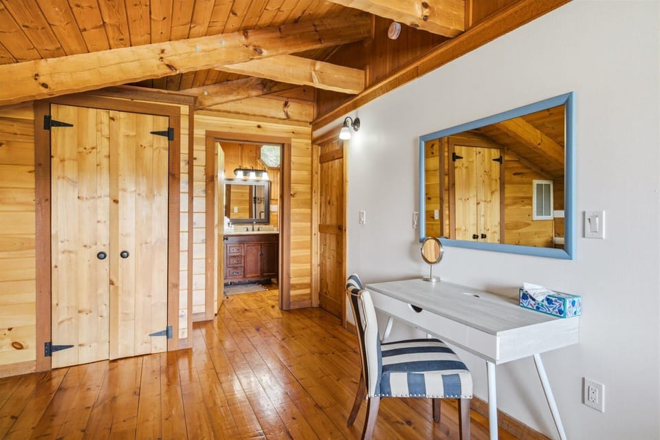 Step into a warm cabin retreat where vaulted wood ceilings and polished floors create a cozy haven. Your private vanity nook awaits with soft lighting and a mirror that reflects the natural charm all around you.