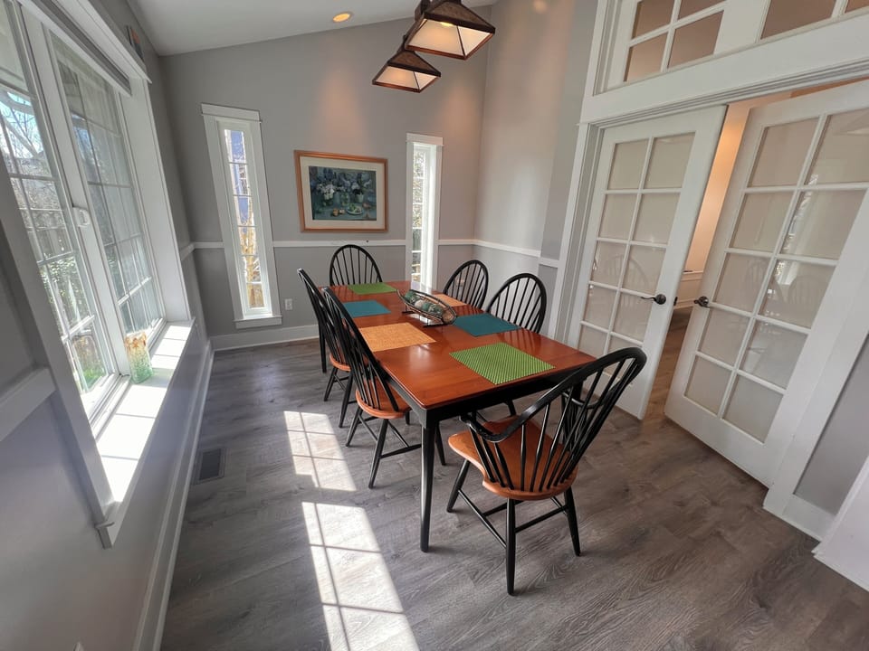 Gather around this warm dining space where natural light streams through tall windows, creating the perfect setting for your morning coffee or evening meals together.